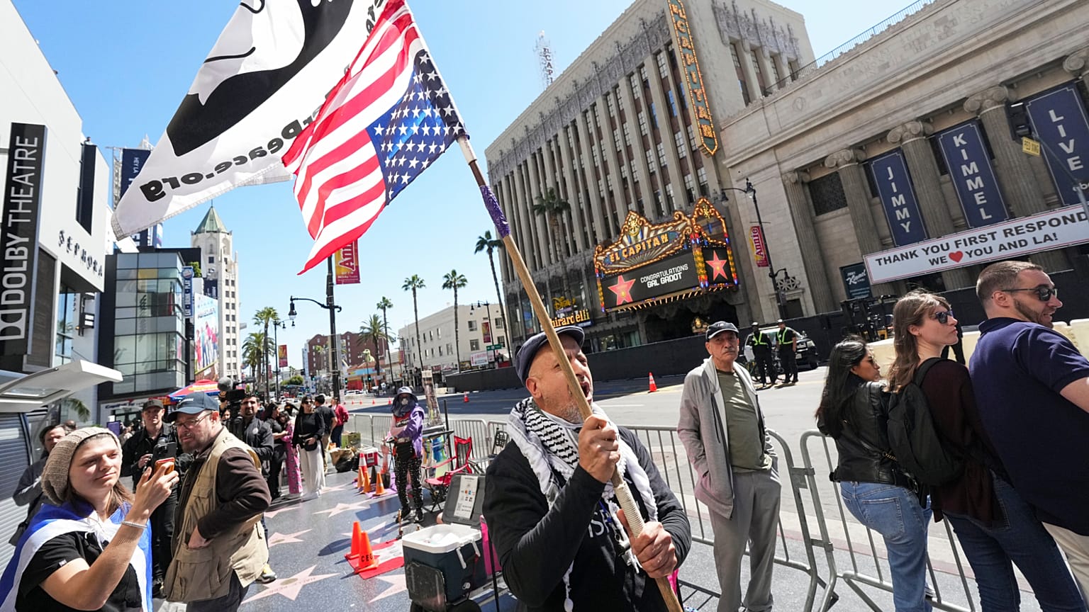 İnsanlar, 18 Mart 2025'te Gal Gadot'un Hollywood Şöhret Yolu'nda bir yıldızla onurlandırıldığı alanın dışında, İsrail-Hamas savaşına atıfta bulunan pankartlar ve bayraklar tutuyor.