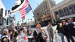 Menschen halten Schilder und Fahnen, die auf den Israel-Hamas-Krieg verweisen, außerhalb des Bereichs, in dem Gal Gadot am 18. März 2025 mit einem Stern auf dem Hollywood Walk of Fame geehrt wurde.