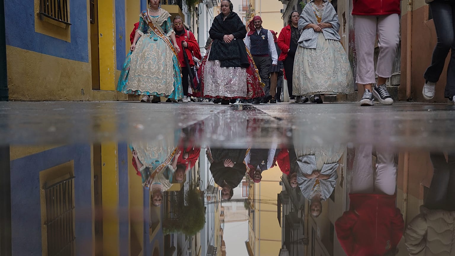 Mujeres vestidas con ropa de los siglos XVIII y XIX, conocidas como falleras, se ven reflejadas en un charco de agua de lluvia, durante el festival de las Fallas en Valencia