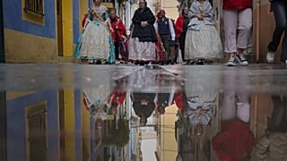 Mujeres vestidas con ropa de los siglos XVIII y XIX, conocidas como falleras, se ven reflejadas en un charco de agua de lluvia, durante el festival de las Fallas en Valencia