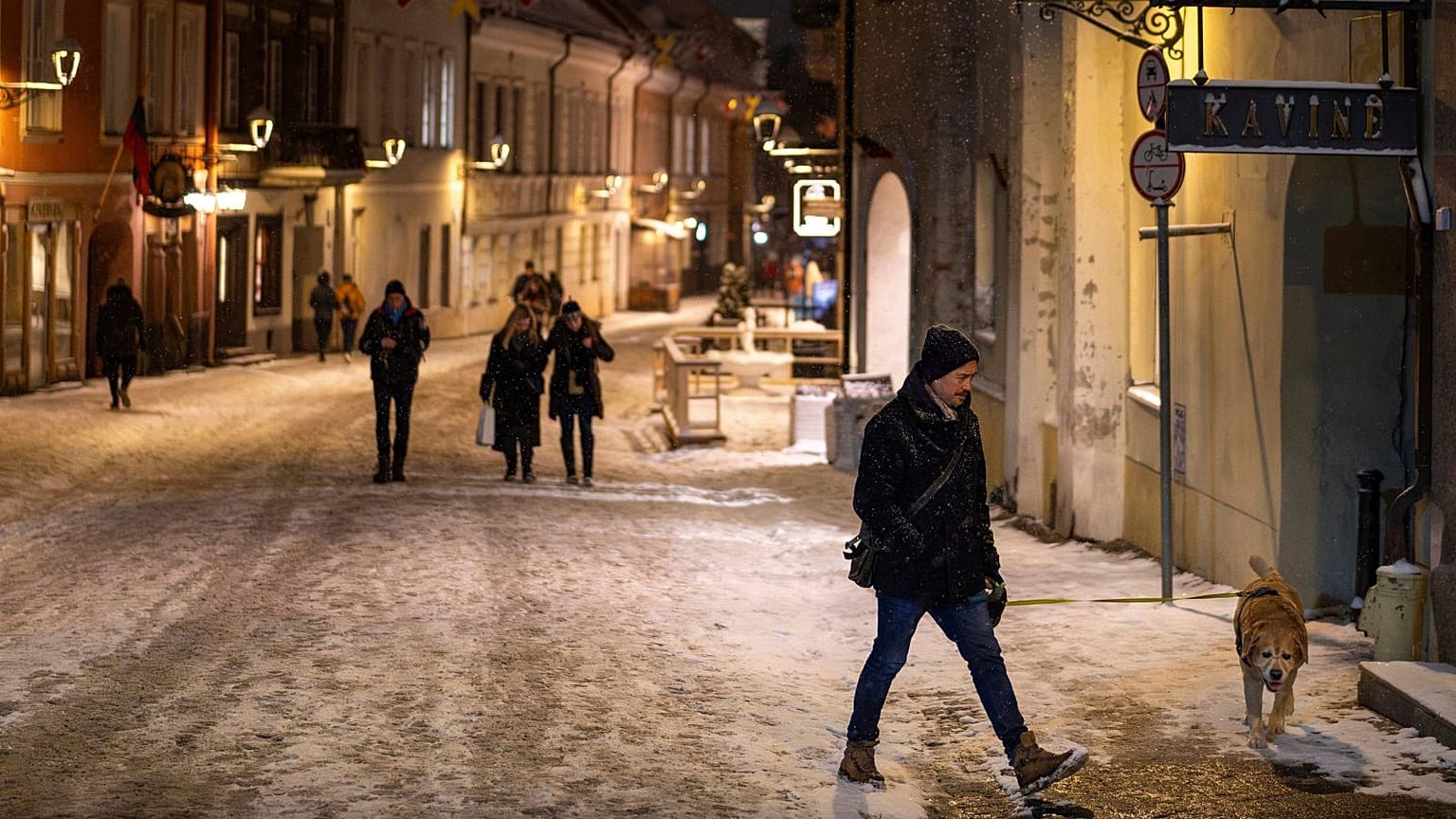 Ένα άτομο με έναν σκύλο περπατάει μέσα στη χιονισμένη Παλιά Πόλη στο Βίλνιους της Λιθουανίας, 17 Φεβρουαρίου 2025.