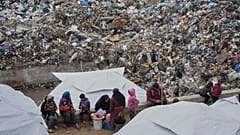 Palestinians displaced by the Israeli air and ground offensive in Gaza sit in a makeshift tent camp inside a landfill, 21 March, 2025