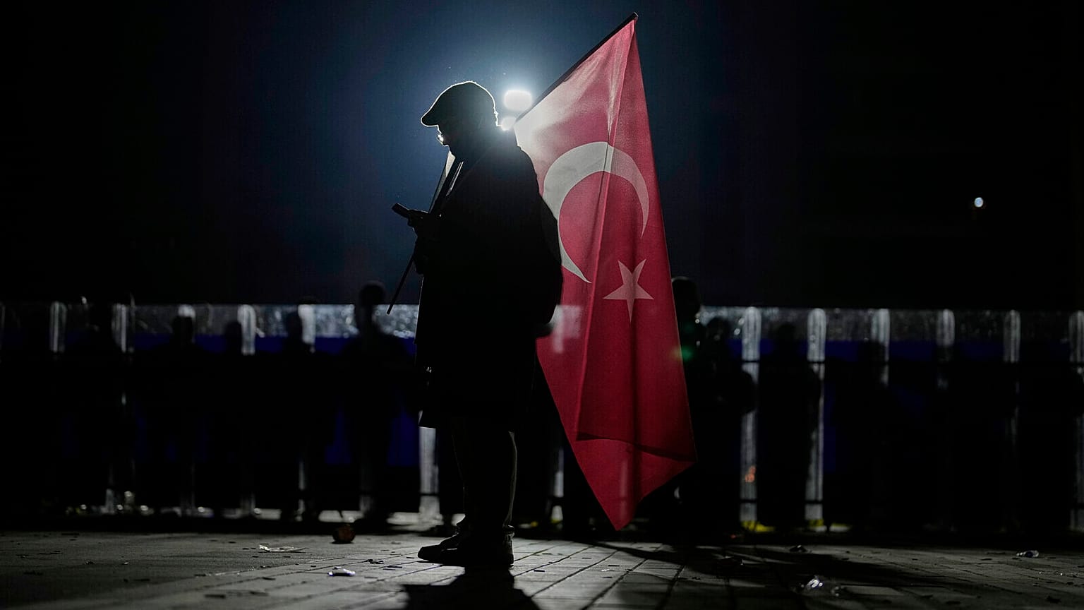 Egy tüntető török zászlót tart, miközben rohamrendőrök őrködnek az Ekrem Imamoglu isztambuli polgármester letartóztatása elleni tüntetésen, a Caglayan bíróság épülete előtt, Isztambulban,