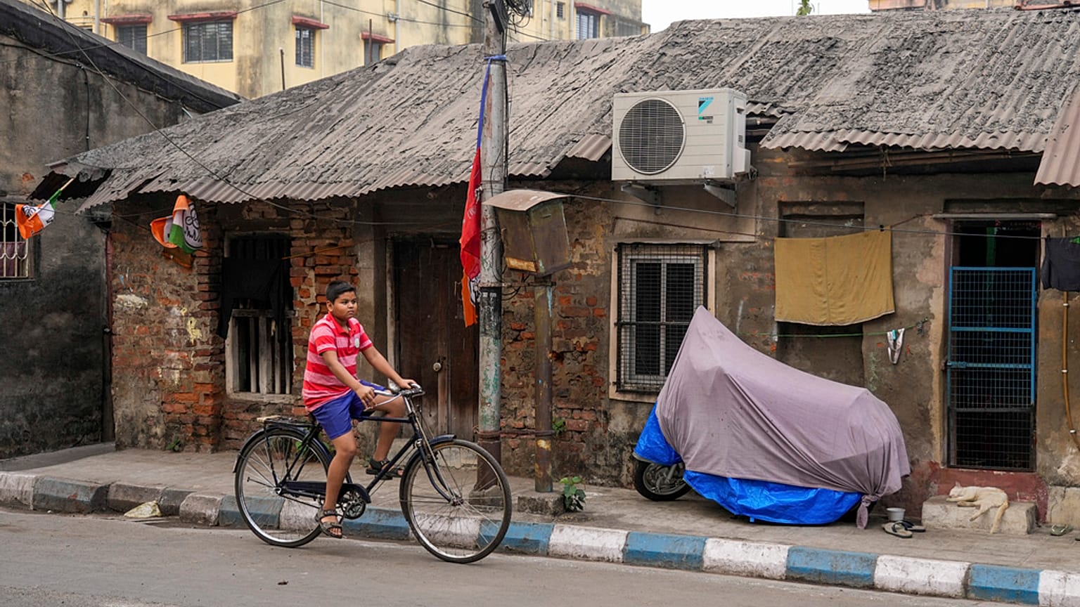 Um rapaz pedala uma bicicleta ao passar por uma cabana de um só piso equipada com ar condicionado em Calcutá, Índia