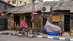 Hindistan'ın Kalküta kentinde bir çocuk, klimayla donatılmış tek katlı bir kulübenin önünden bisikletiyle geçiyor