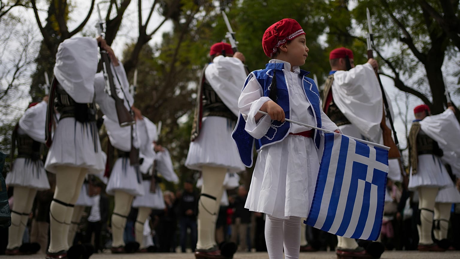 Uma criança vestida como um Evzonas segura uma bandeira grega diante da Guarda Presidencial em Atenas, antes de um desfile que marca o Dia da Independência da Grécia, na terça-feira, 25 de março de 2025.