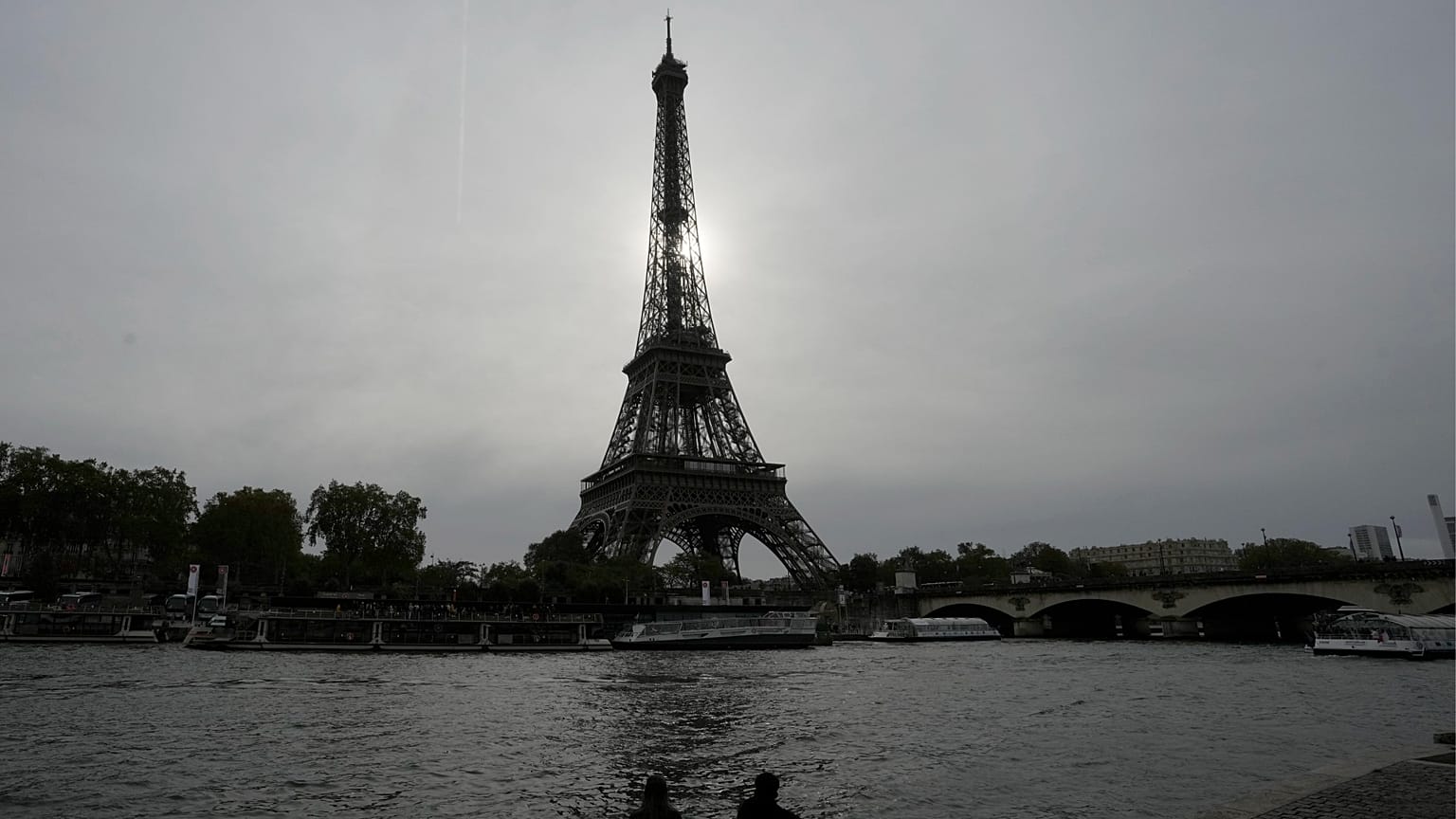 A couple sits by the river's embankment with the Eiffel Tower in the background in Paris, France, Thursday, Oct. 26, 2023. 