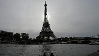 A couple sits by the river's embankment with the Eiffel Tower in the background in Paris, France, Thursday, Oct. 26, 2023.
