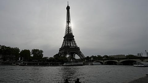 A couple sits by the river's embankment with the Eiffel Tower in the background in Paris, France, Thursday, Oct. 26, 2023. 