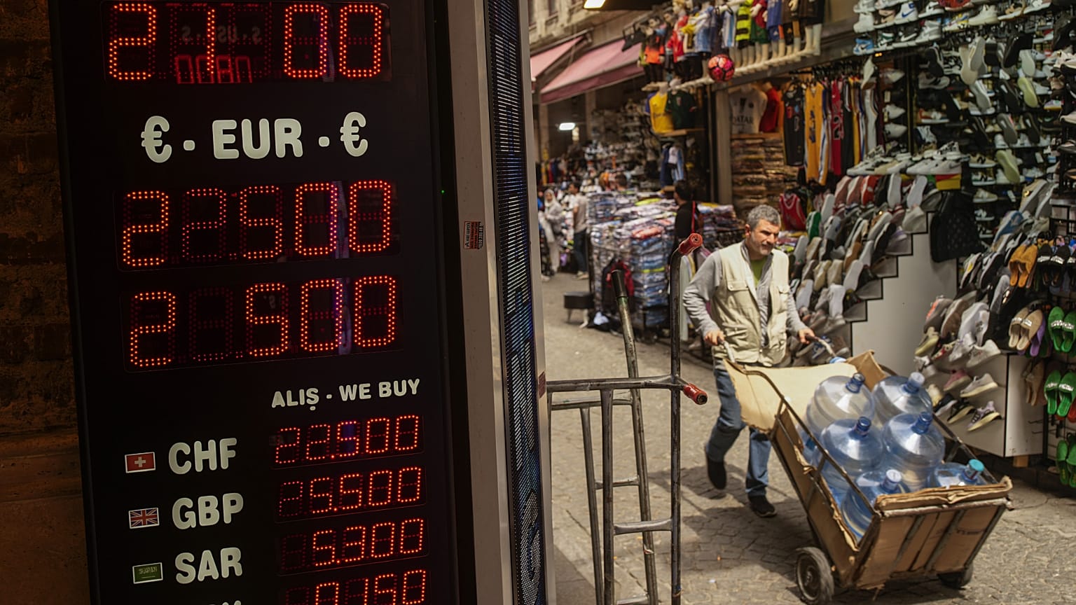 Un uomo trasporta bottiglie d'acqua accanto a un negozio di cambio valuta nell'area commerciale di Eminönü, a Istanbul