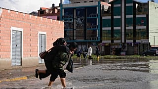 La gente cruza una calle inundada después de fuertes lluvias en El Alto, Bolivia, el domingo 23 de marzo de 2025.
