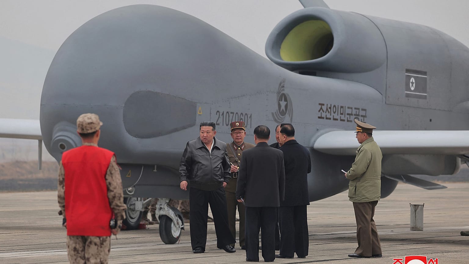 O líder norte-coreano Kim Jong-un, no centro à esquerda, ao lado do que parece ser um grande drone de reconhecimento num local não revelado na Coreia do Norte.