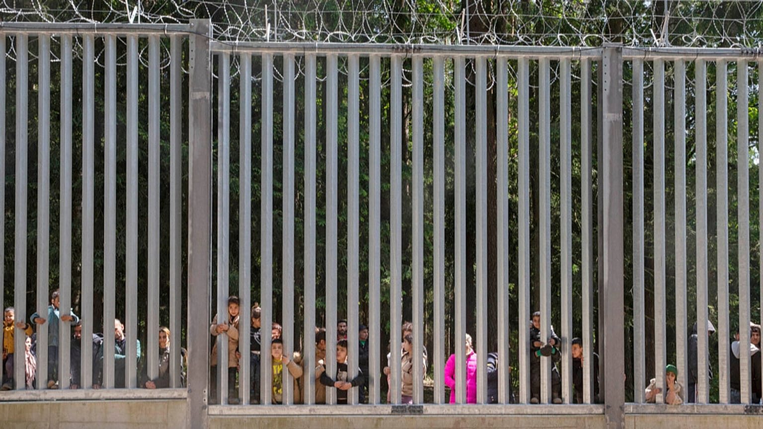 Persone in cerca di asilo guardano attraverso le ringhiere del muro che la Polonia ha costruito al confine con la Bielorussia a Bialowieza, in Polonia, il 28 maggio 2023.