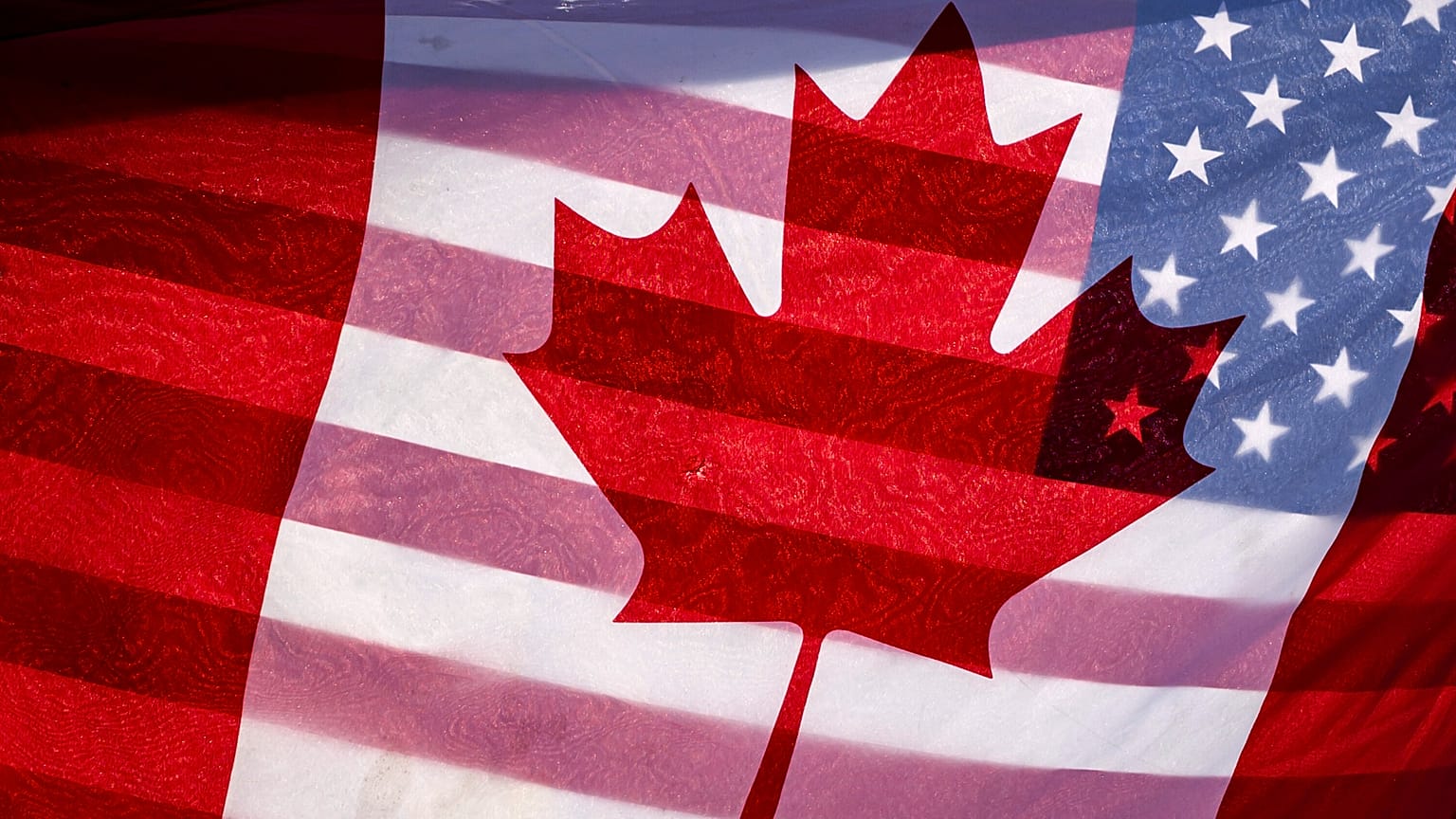 Güneş ışığı, 1 Şubat 2025 tarihinde Ottawa'daki Parlamento Binası önünde bir protestocu tarafından bir arada tutulan Kanada ve Amerika Birleşik Devletleri bayraklarının arasından parlıyor.