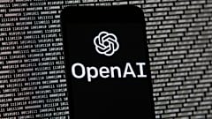 El logotipo de OpenAI aparece en un teléfono móvil frente a una pantalla de ordenador con datos binarios aleatorios, el 9 de marzo de 2023, en Boston.