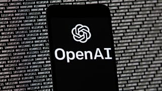 El logotipo de OpenAI aparece en un teléfono móvil frente a una pantalla de ordenador con datos binarios aleatorios, el 9 de marzo de 2023, en Boston.