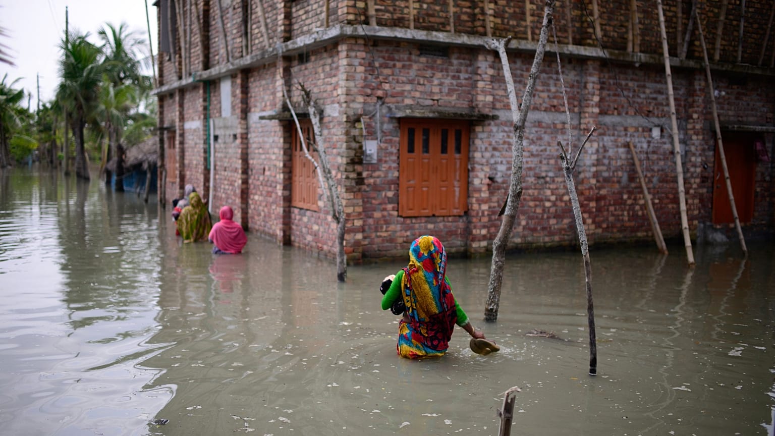 Aldeões atravessam águas até à cintura para chegar às suas casas em Pratap Nagar, Bangladesh, a 5 de outubro de 2021. A água salgada chega ao interior do país à medida que o Bangladesh enfrenta mais ciclones.