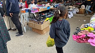 طفلة فلسطينية تنظر لملابس العيد في سوق شعبي بدير البلح، غزة بتاريخ 