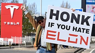 Egy tüntető egy plakátot tart, miközben részt vesz a Tesla Takedown Global Day of Action-en egy Tesla-kereskedés közelében Londonban, 2025. március 29-én.