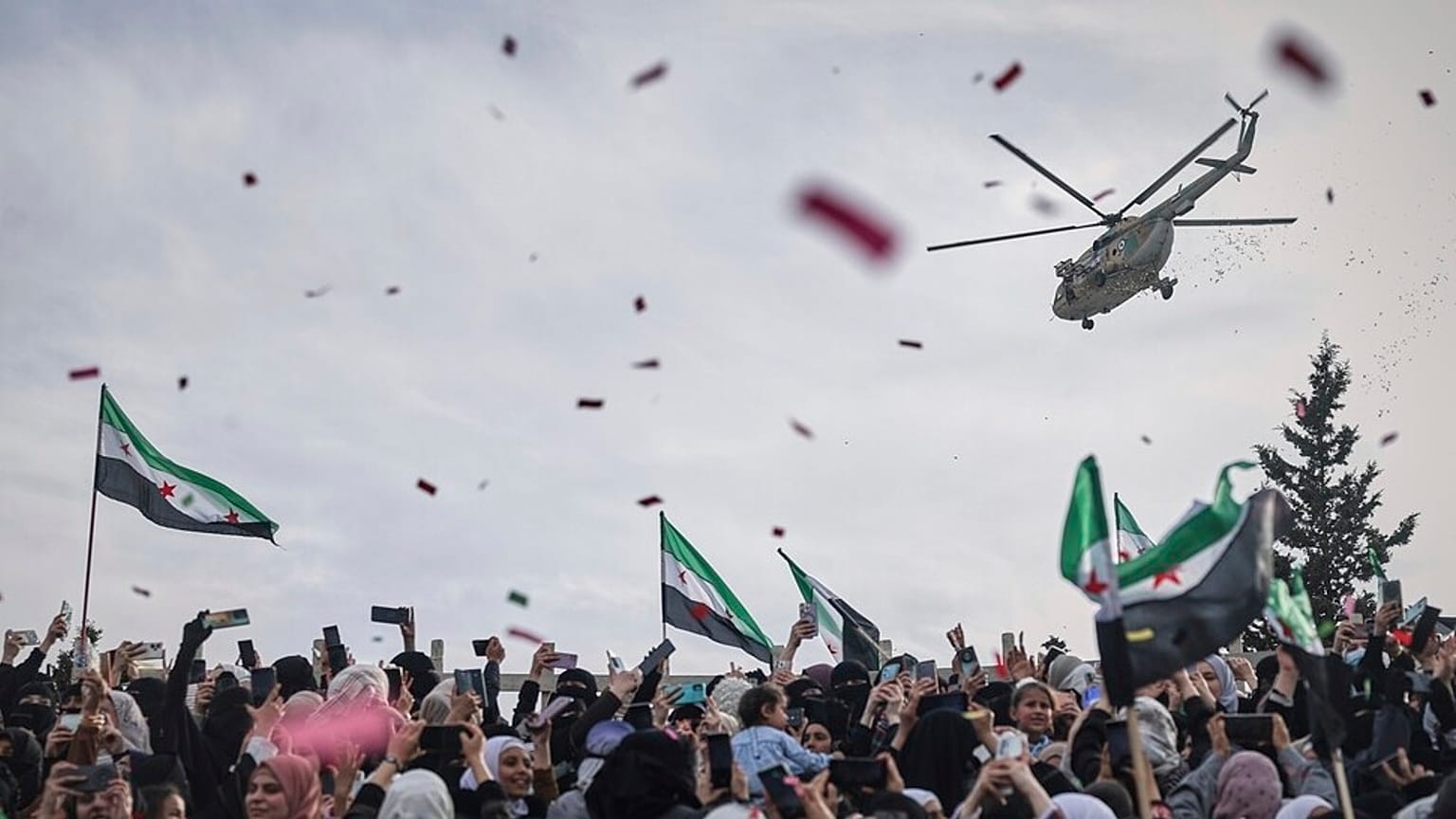Des confettis et des fleurs sont largués d'un hélicoptère militaire sur la foule lors de la célébration de la victoire des forces rebelles sur l'armée d'Al-Assad à Idlib, en Syrie, le 28 mars 2025.