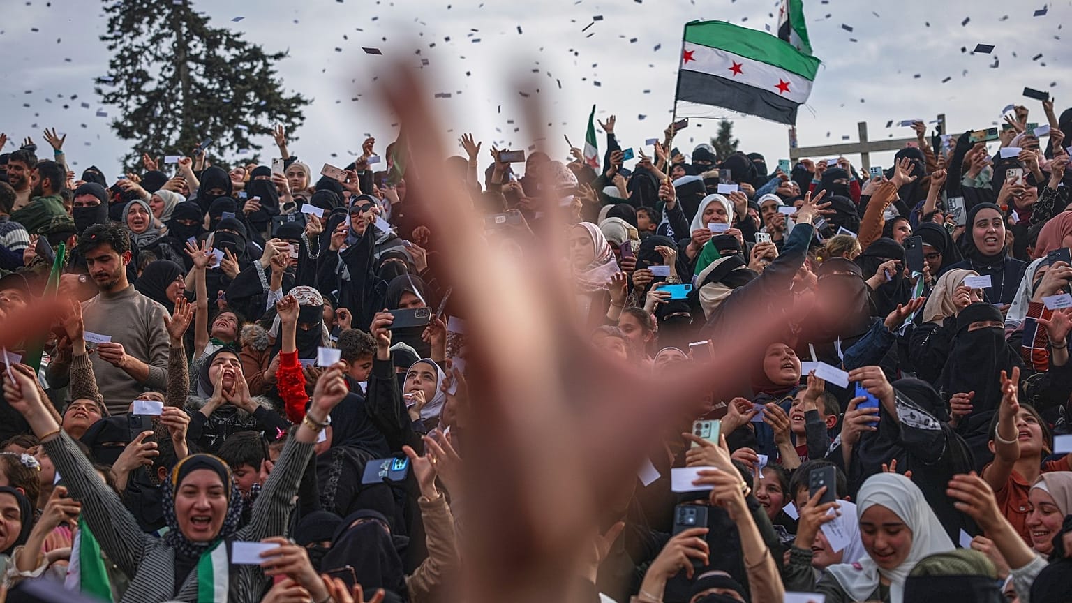 Des bonbons et des fleurs sont largués d'un hélicoptère militaire sur la foule lors d'une célébration marquant le 10e anniversaire de la victoire sur l'armée de Bachar al-Assad à Idlib.