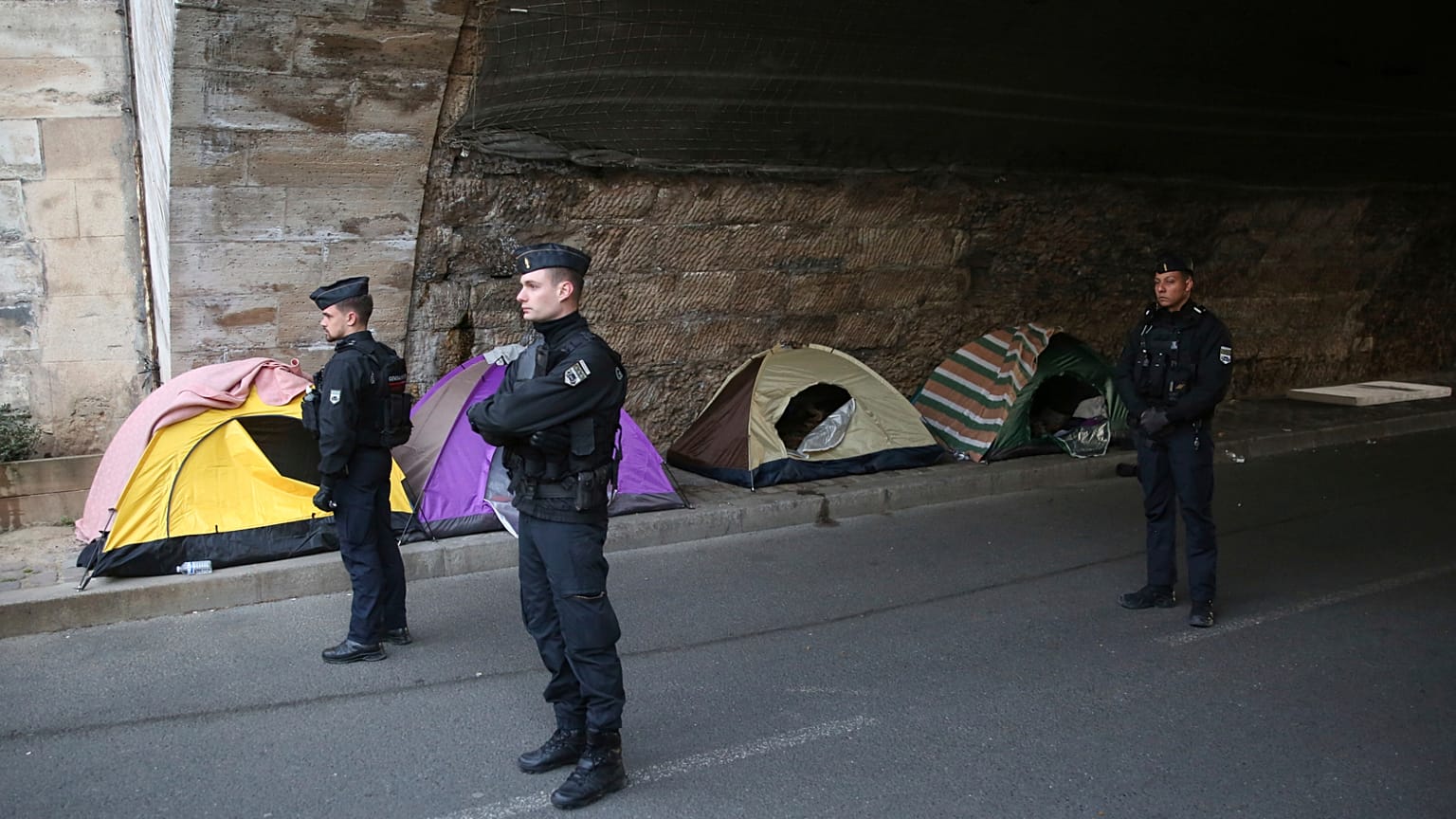 Polis memurları, 1 Nisan 2025 Salı günü Paris'teki Seine Nehri boyunca göçmenleri tahliye eden yetkililerin yanında çadırların önünde duruyor.