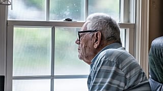 Un homme âgé regarde par la fenêtre.