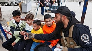 شرطي سوري يسلم الحلوى للأطفال في اليوم الأخير من عطلة عيد الفطر في مخيم اليرموك للاجئين الفلسطينيين في دمشق