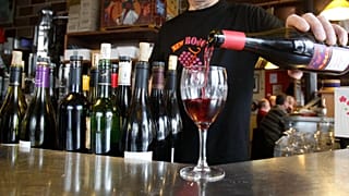 Un camarero sirve una copa de vino a un cliente en un bar.