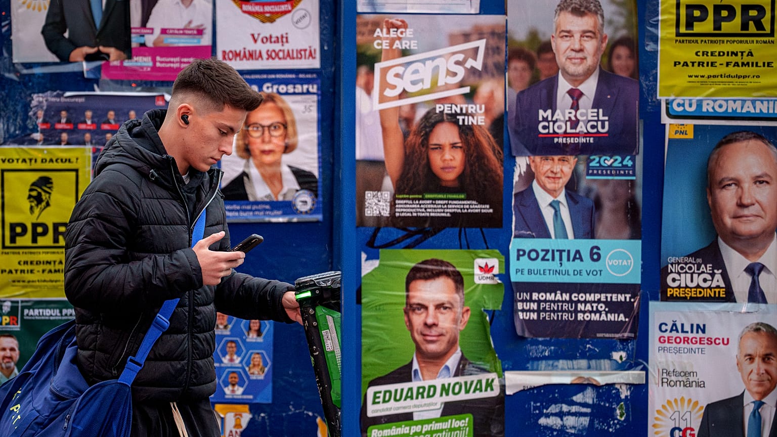 A young man stands by panels displaying electoral posters ahead of the presidential election in Bucharest, 22 November, 2024