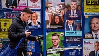 A young man stands by panels displaying electoral posters ahead of the presidential election in Bucharest, 22 November, 2024