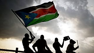 ARQUIVO - Sudaneses do Sul acenam com a bandeira nacional e aplaudem no primeiro jogo de futebol nacional do Sudão do Sul depois de o país ter declarado a sua independência, em Juba, a 10 de julho de 2011.