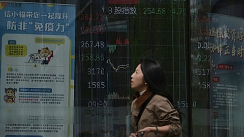 A woman walks by an electronic board displaying shares trading index at a brokerage house, in Beijing, 7 April 2025. 