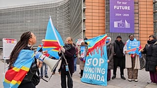 Egy Kongó-párti tüntető "Kongó nem eladó" feliratú táblát tart az Európai Tanács épülete előtt Brüsszelben, 2025. március 17-én.