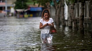 Uma mulher tailandesa está ocupada com o seu telemóvel enquanto atravessa as águas das cheias nos arredores de Banguecoque, na Tailândia, na segunda-feira, 28 de novembro de 2011.