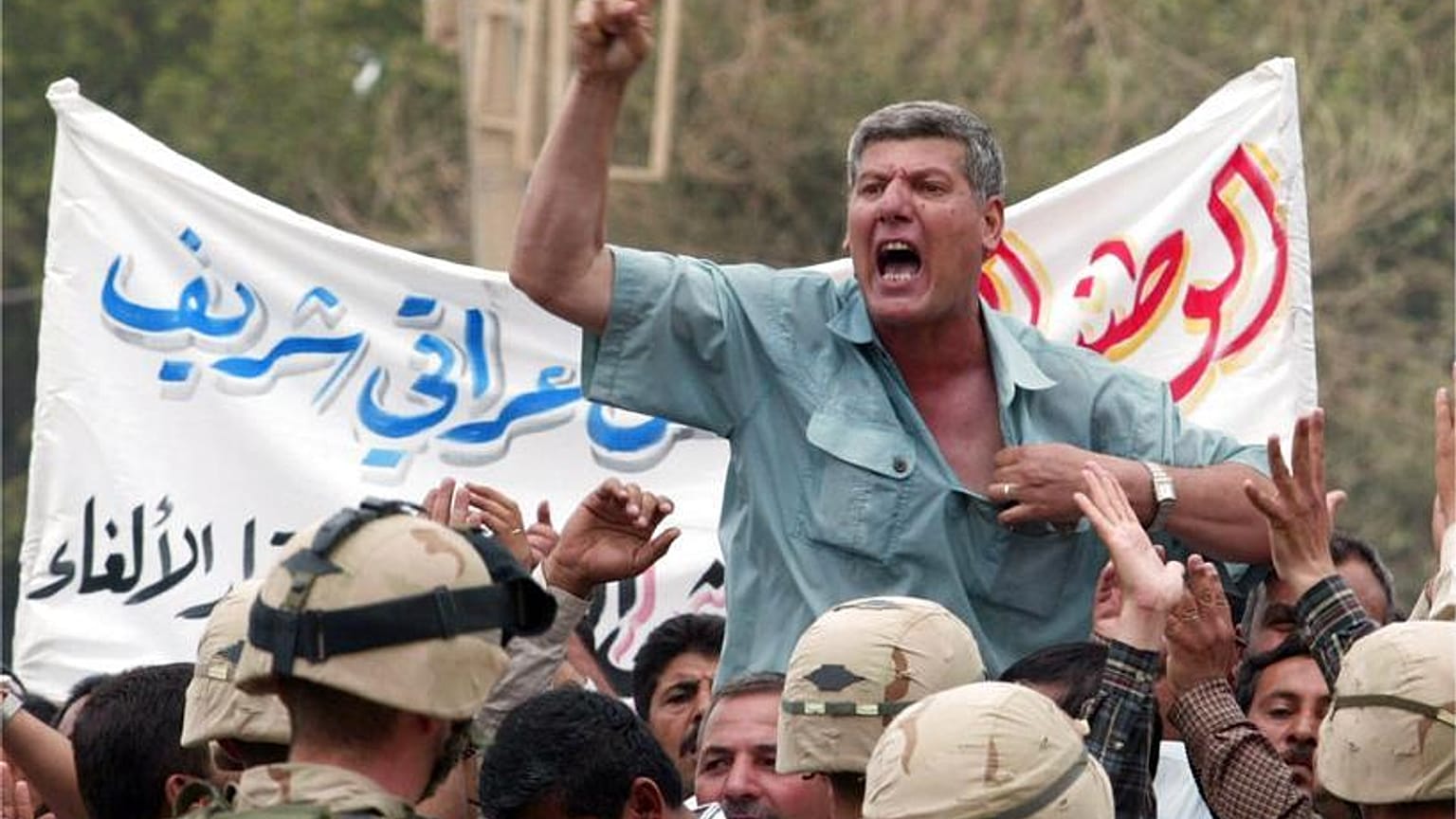جندي سابق بالجيش العراقي يصرخ بشعارات بينما يقف الجنود الأمريكيون خارج القصر الجمهوري في بغداد يوم الاثنين 2 يونيو 2003.