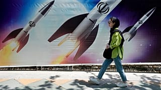 A woman walks past a banner showing missiles being launched, in northern Tehran, Iran.