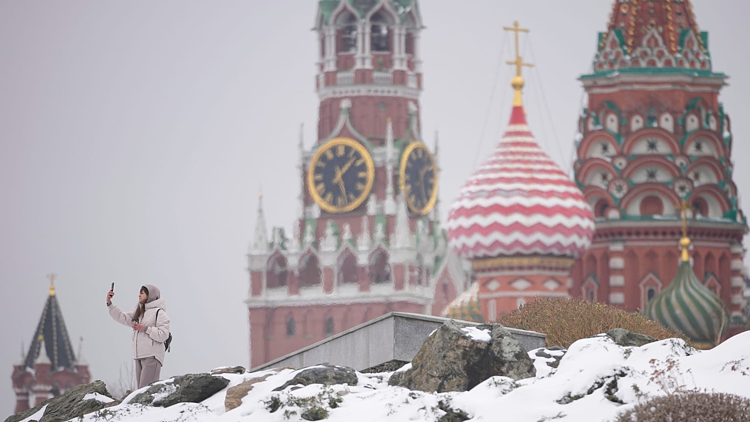 A woman takes selfies at the Zaryadye park with the Kremlin and St. Basil's Cathedral in the background, after a snowfall in Moscow, 7 April 2025