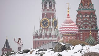 A woman takes selfies at the Zaryadye park with the Kremlin and St. Basil's Cathedral in the background, after a snowfall in Moscow, 7 April 2025