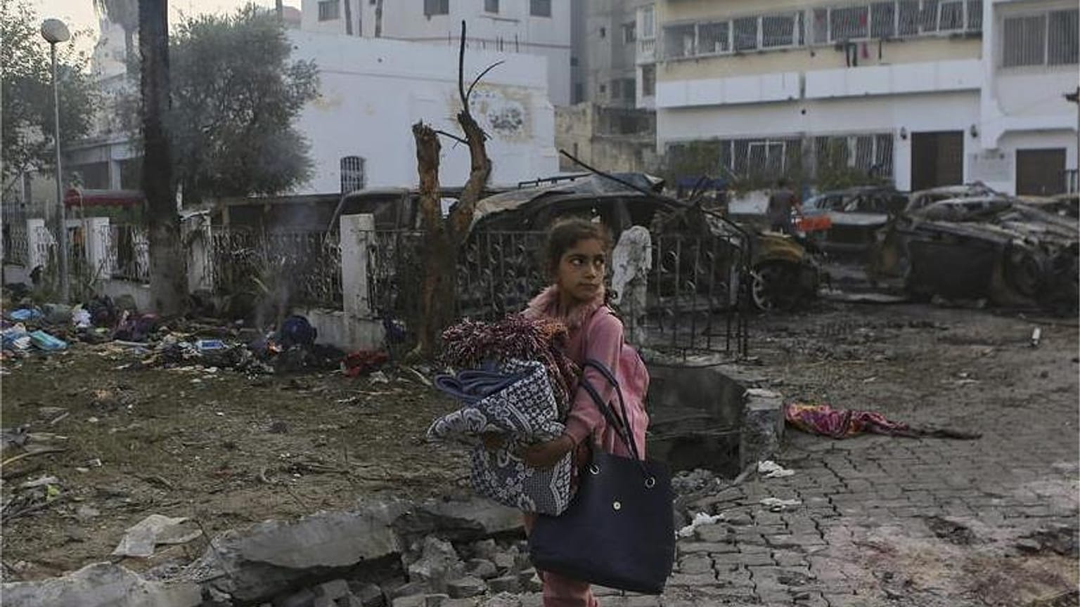 فتاة فلسطينية تحمل بطانيات وهي تمشي أمام موقع انفجار مميت في المستشفى الأهلي, في مدينة غزة, الأربعاء, أكتوبر. 18, 2023.