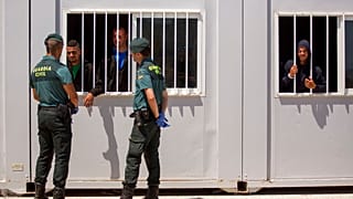 Funkcjonariusze Gwardii Cywilnej rozmawiają z migrantami uwięzionymi w prowizorycznym ośrodku ratunkowym w porcie Barbate, w południowej Hiszpanii.