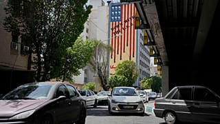Vehículos circulan delante de un mural contra Estados Unidos en el centro de Teherán, Irán, el domingo 13 de abril de 2025. (AP Photo/Vahid Salemi)