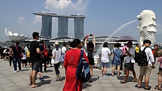 Tourists take photographs next to the Merlion in front of the Marina Bay Sands, 7 June, 2018