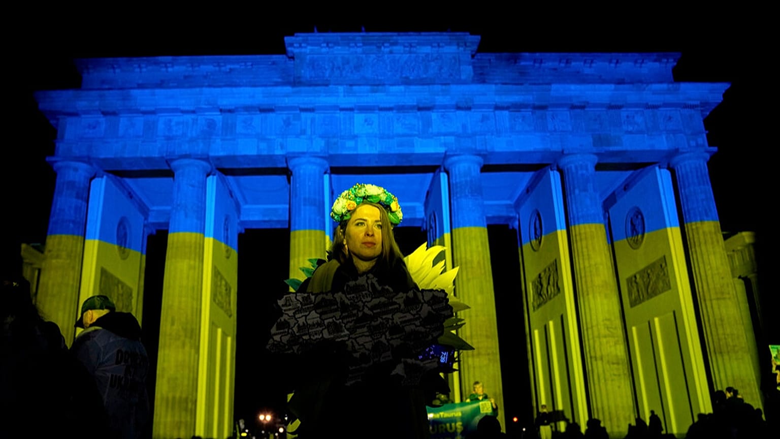 Manifestantes chegam à Porta de Brandemburgo, iluminada com as cores da Ucrânia, durante uma manifestação contra a guerra da Rússia contra a Ucrânia.