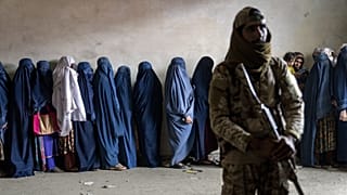 Egy tálib harcos őrködik, miközben nők várakoznak, hogy megkapják a humanitárius segélyszervezet által kiosztott élelmiszeradagokat Kabulban, 2023. május 23.
