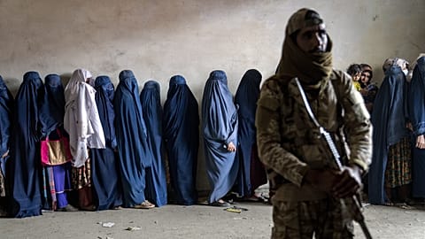 Egy tálib harcos őrködik, miközben nők várakoznak, hogy megkapják a humanitárius segélyszervezet által kiosztott élelmiszeradagokat Kabulban, 2023. május 23.