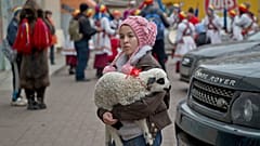 Un bambino mendicante tiene in mano un agnello mentre gli abitanti del villaggio di Dofteana, nella Romania settentrionale, alcuni dei quali indossano pellicce di orso, si vedono sullo sfondo, mentre eseguono un rituale per le festività natalizie a Bucarest.