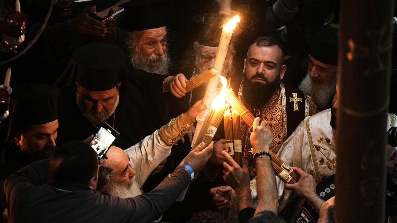 O Patriarca Ortodoxo Grego de Jerusalém, Teófilo III, à esquerda, acende velas para os peregrinos cristãos durante a cerimónia do Fogo Sagrado, na Igreja do Santo Sepulcro, 19.04.2025