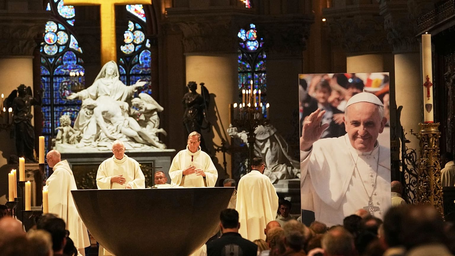 Az emberek misén vesznek részt a Notre-Dame székesegyházban, ahol egy plakát Ferenc pápát ábrázolja.