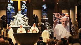 Menschen nehmen an einer Messe in der Kathedrale Notre Dame teil, wo ein Plakat Papst Franziskus zeigt.